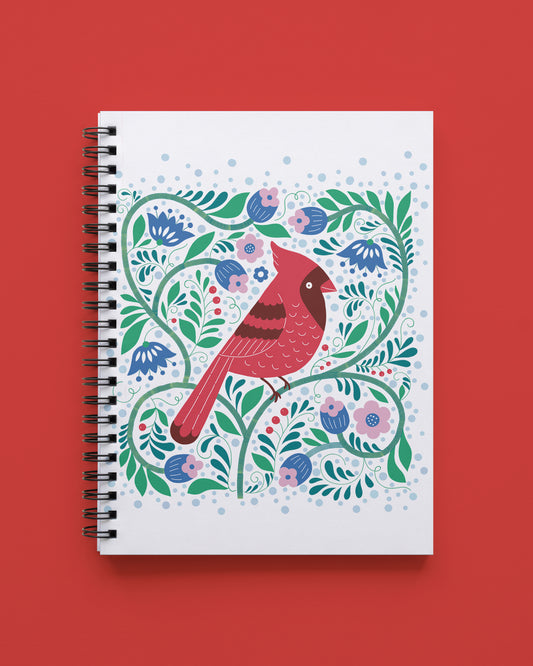 Wire bound notebook with a white cover showing a red cardinal among blue and pink flowers, green vines, and light blue dots, shown on a red background