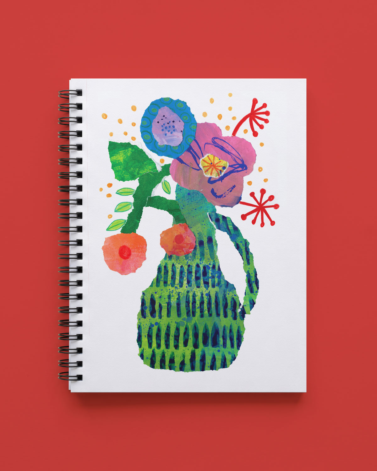 Wire bound notebook with a white cover showing a green patterned pitcher holding mauve, blue, and coral collage-style flowers with red starburst accents, shown on a red background