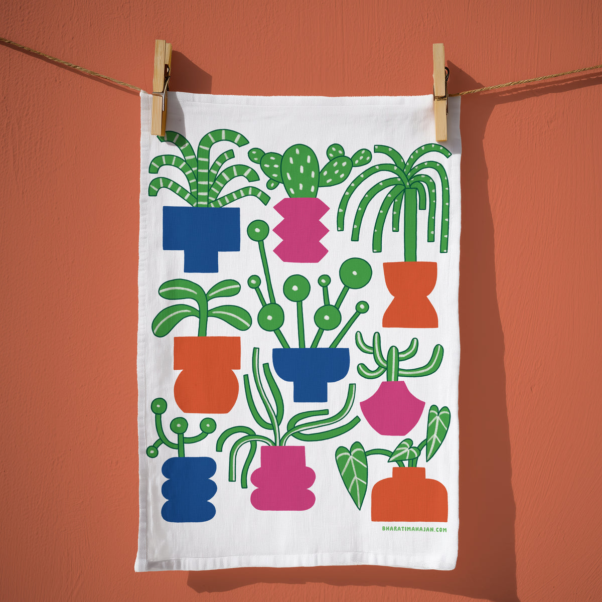 Kitchen towel with a colorful illustration of potted houseplants and cacti in blue, pink, and orange pots, hanging from wooden clothespins