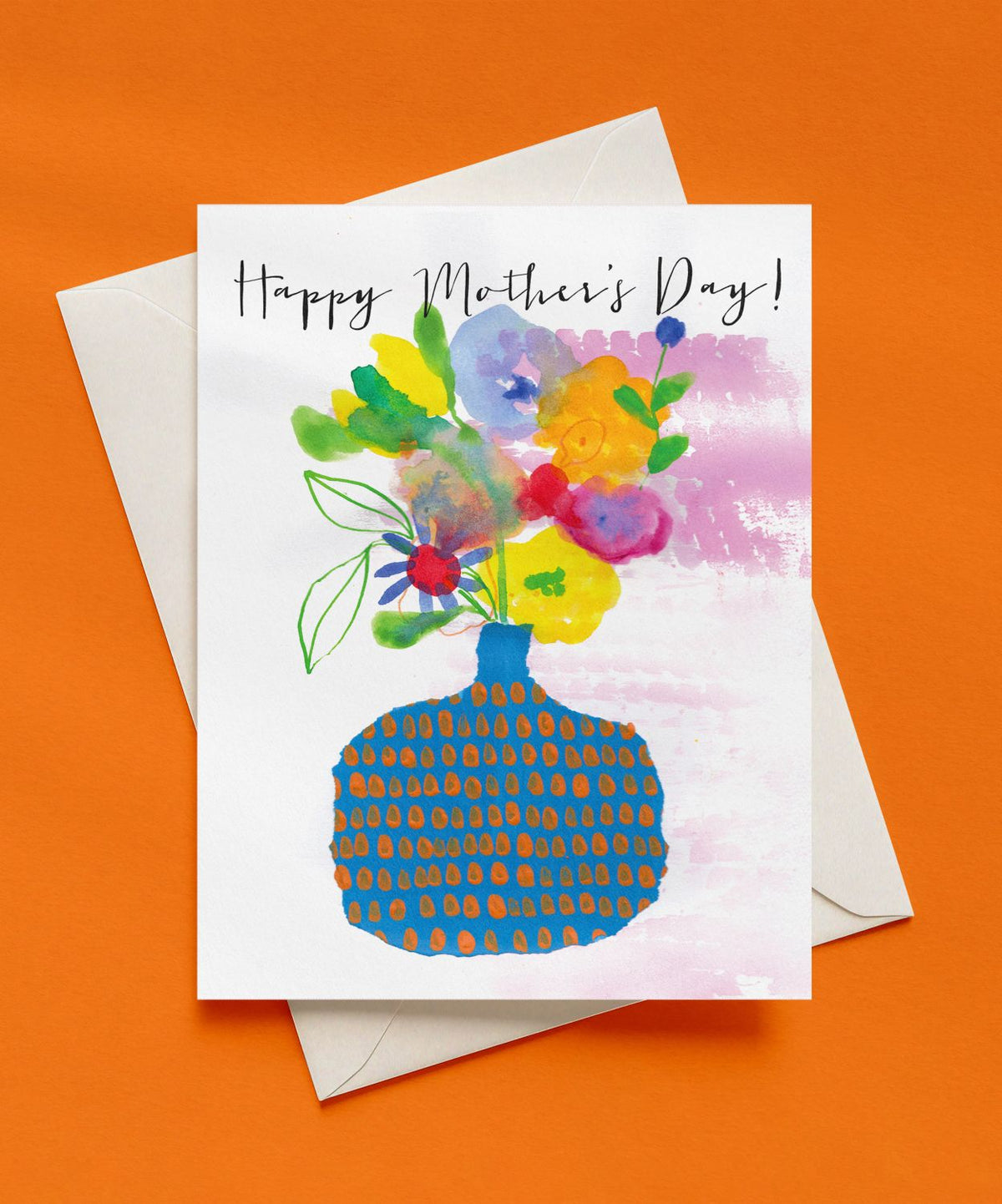 Happy Mother’s Day card with dark script lettering above a watercolor bouquet of yellow, orange, pink, and lavender flowers in a blue vase with orange dots, shown with a cream envelope on an orange background