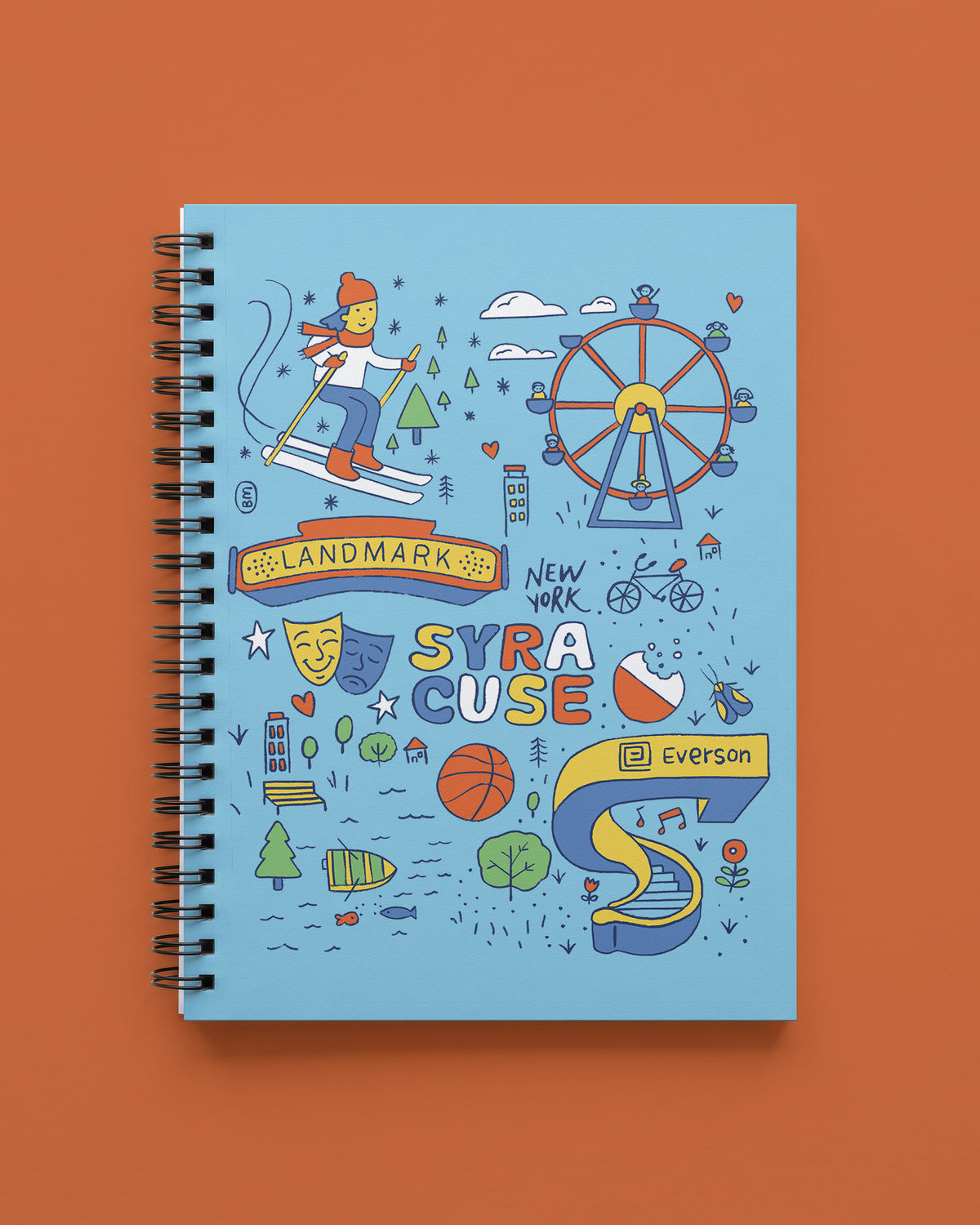 Wire bound notebook with a light blue cover and a hand-drawn Syracuse, New York design featuring a skier, Ferris wheel, Landmark Theatre sign, theater masks, and Everson Museum, shown on a terracotta background