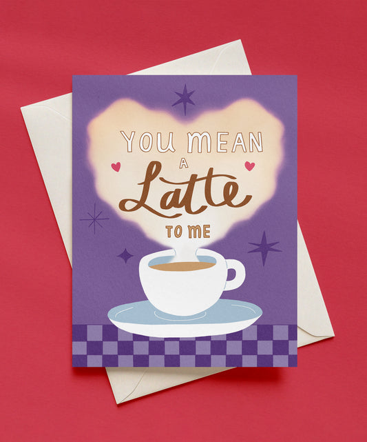 You Mean a Latte to Me greeting card with a white latte cup and a glowing heart of steam on a purple background with a checkered border, shown with a cream envelope